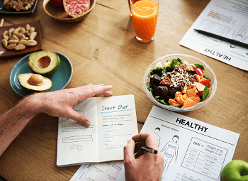 Man taking notes about eating healthy with several healthy foods around him on a table